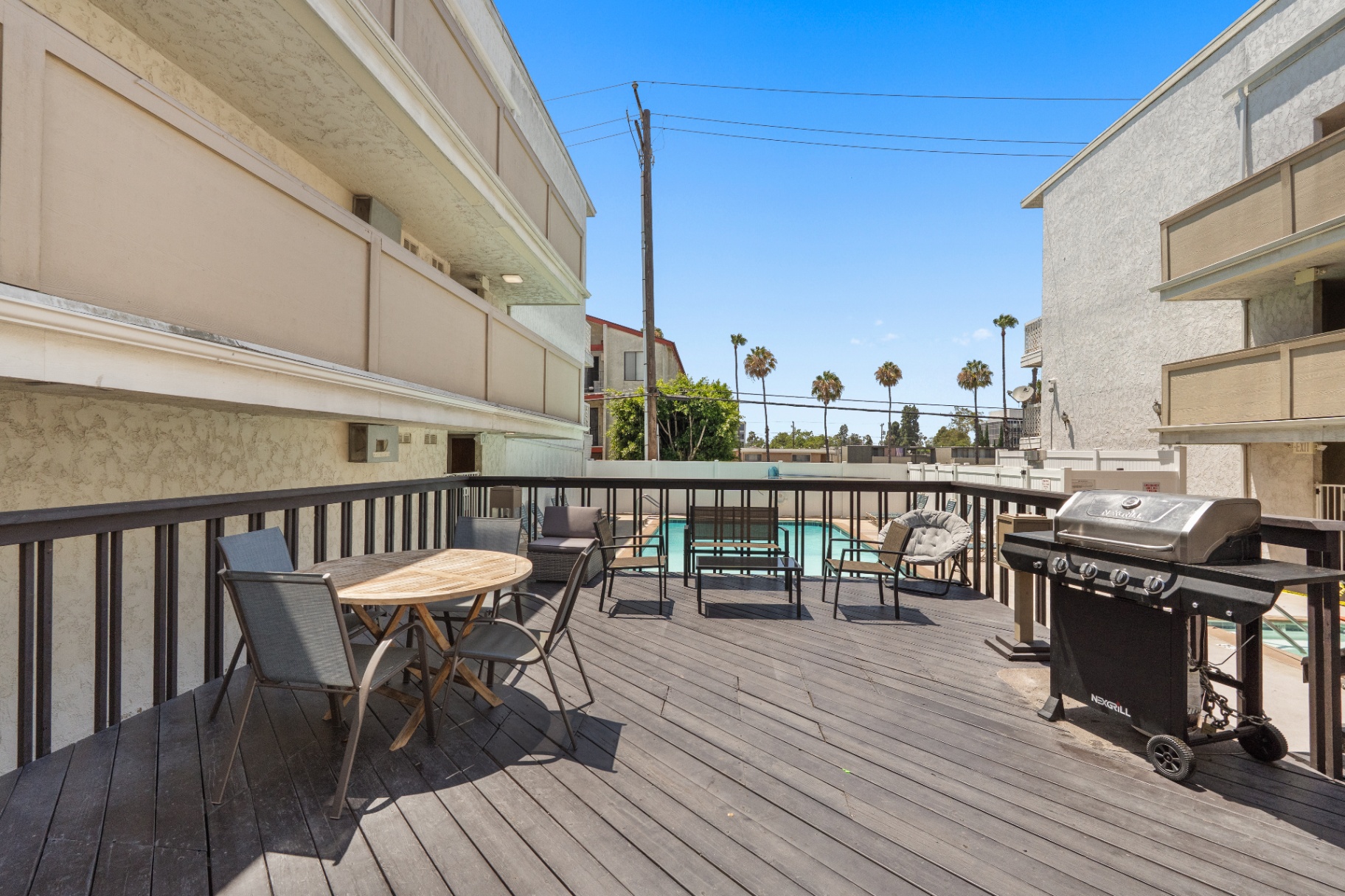 Community sun deck with lounge seating, dining table, and gas BBQ above the pool