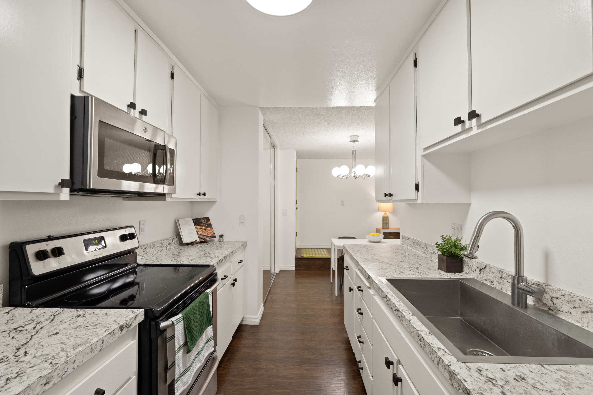 Galley kitchen with stainless steel sink, electric range, microwave, and view toward the dining area