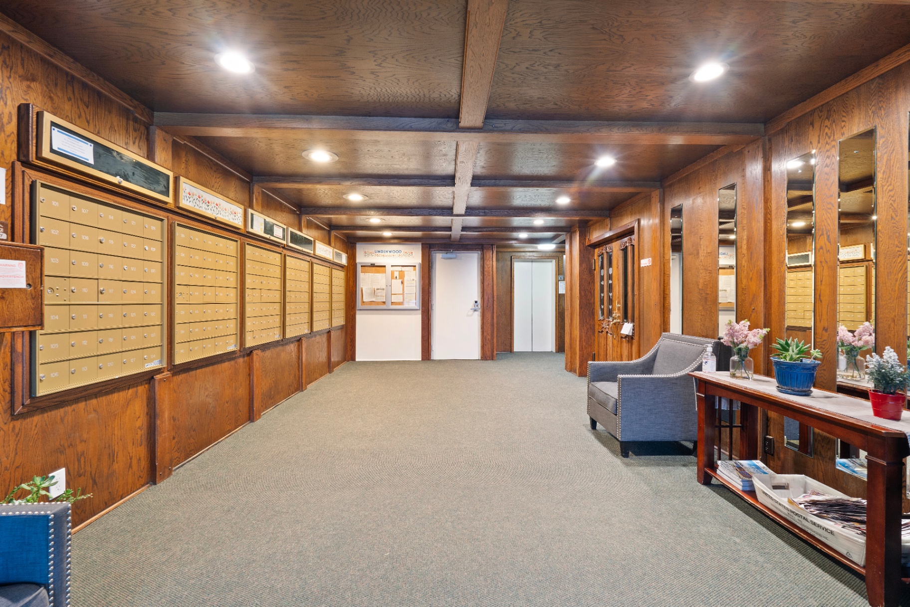 Warm wood-paneled lobby entryway with mailboxes, seating, and elevator